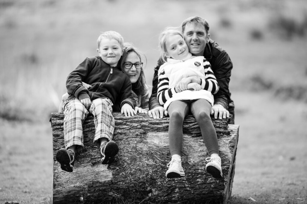 mum dad and children sitting on a fallen down tree in Knole Park Sevenoaks during a photoshoot